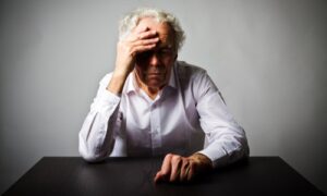 sad-senior-man-sitting-table-against-gray-background